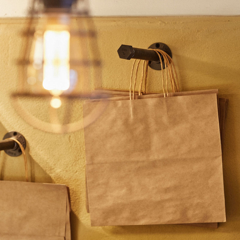 Simple and practical clothes hook made from dark water pipes attached to wall for bags