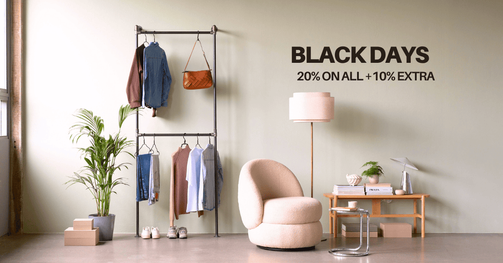 Heller Raum mit Garderobenständer, Kleidung, Pflanze, Sessel, Stehlampe und Schreibtisch mit Dekoration vor heller Wand mit Werbetext