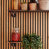Wall mounted oak shelves made with dark iron supports for storing plants and oils in kitchen